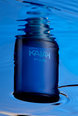 Frasco azul-escuro da fragrância Kaiak Pulso flutuando em água azul, com reflexos ondulados.