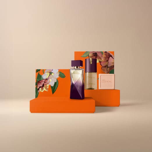 Presente Natura Essencial Exclusivo Feminino, contendo 1 Deo Parfum, 1 Desodorante Corporal e 1 Sabonete em Barra. Os itens estão sobre caixas de presentes laranja com estampa de flores em fundo bege