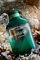 Frasco de Kaiak Aventura masculino em verde sobre pedras molhadas com água corrente e respingos.