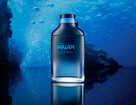 Frasco da fragrância Kaiak Oceano masculino em vidro azul. Fundo marinho com bolhas e reflexo sobre superfície brilhante.