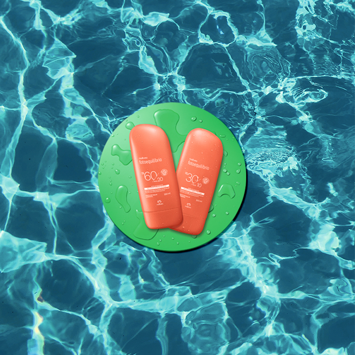 Protetor solar laranja sobre círculo verde com gotas d'água. Fundo azul piscina com textura de água.