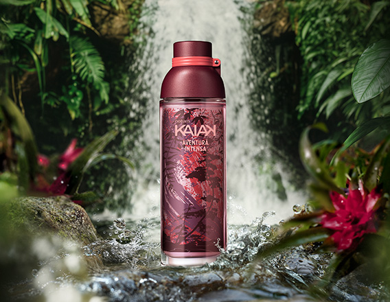 Frasco de Kaiak Aventura Intensa feminino em vermelho sobre pedras na frente de uma cachoeira cercada por folhagens.