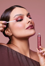 Foto de mulher com cabelos castanhos e presos aplicando o produto Natura Una nas pálpebras, em fundo rosa-claro.