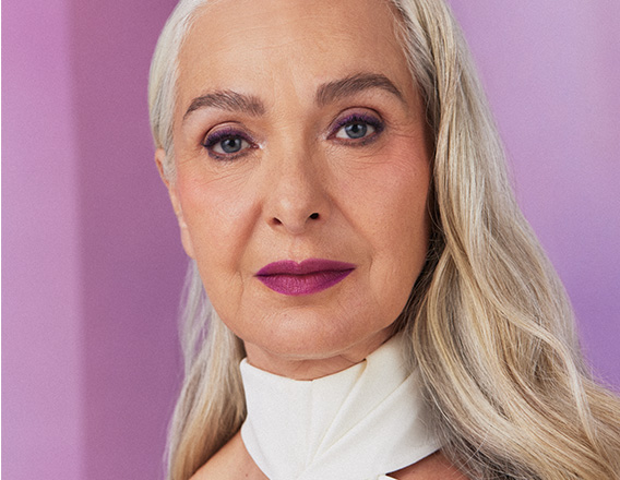 Foto de mulher de cabelos grisalhos e soltos, em fundo lilás.