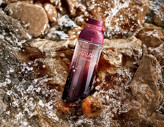 Frasco de Kaiak Aventura feminino em verde sobre pedras molhadas com água corrente e respingos.