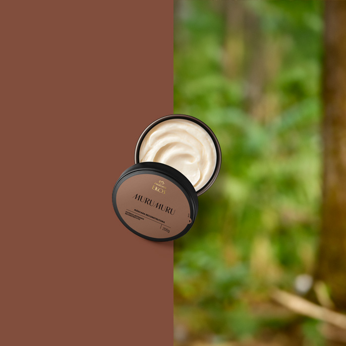 Pote aberto da Máscara Reconstrutora Murumuru Ekos, com creme bege de textura cremosa, está sobre fundo dividido entre marrom e floresta desfocada ao fundo.