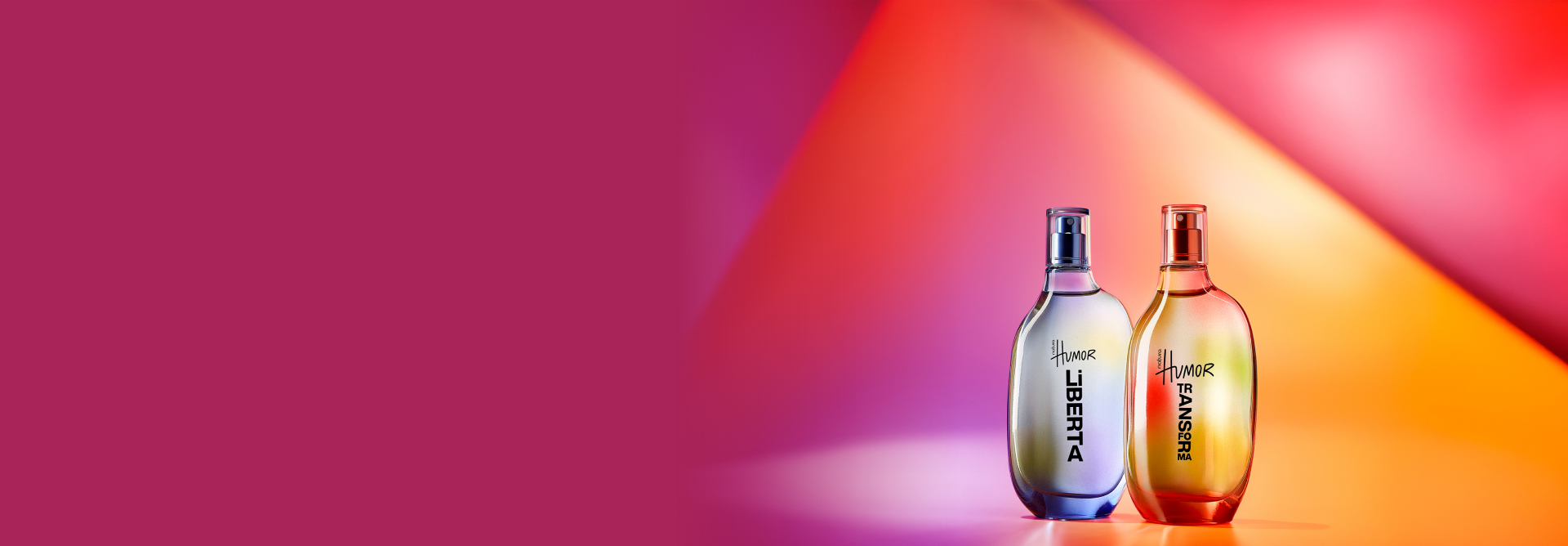 Frascos de fragrâncias Natura Humor nas cores lilás e laranja, em fundo em tons de rosa, vermelho e laranja.