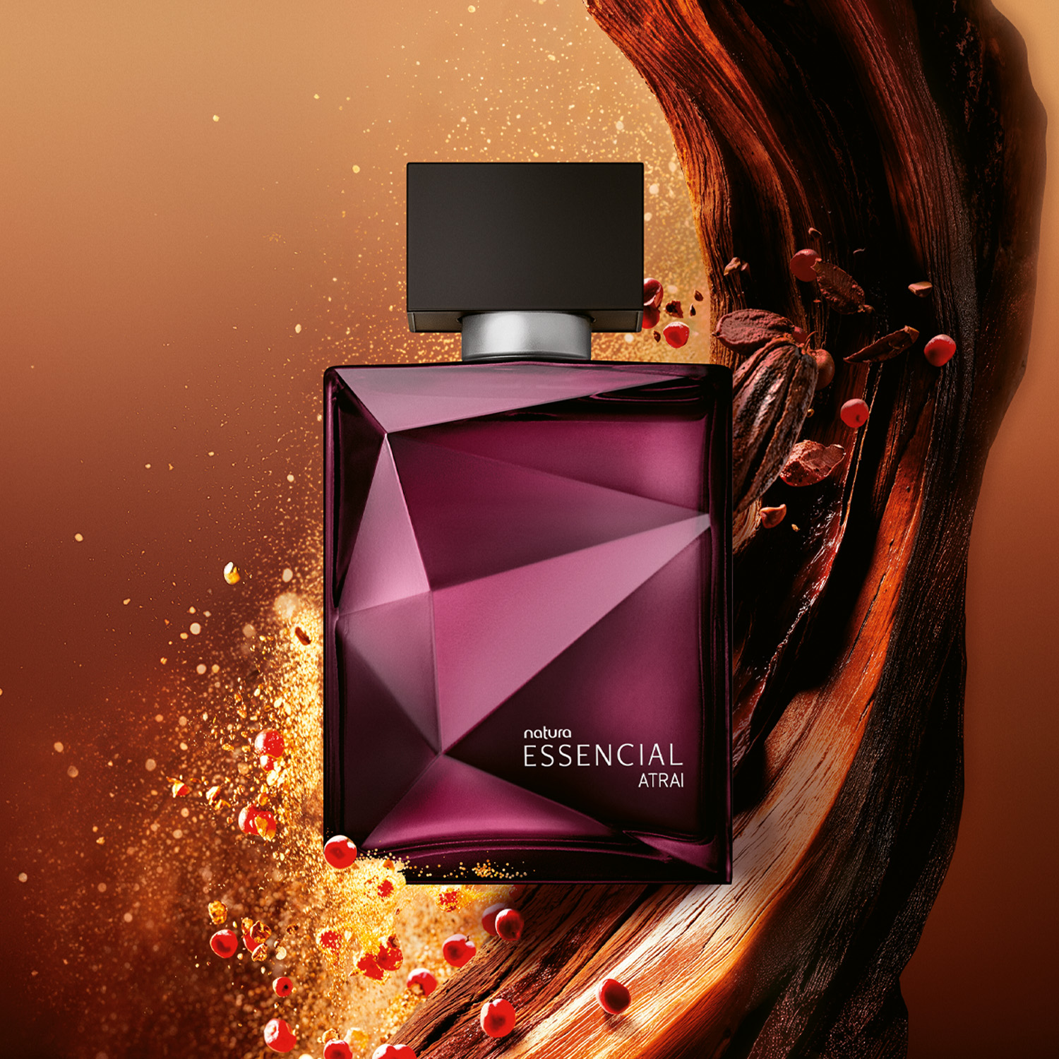 Frasco Deo Parfum Essencial Atrai Masculino em tons de vinho e prata em destaque sobre madeiras e pimenta rosa, elementos que remetem aos ingredientes. Fundo alaranjado. 