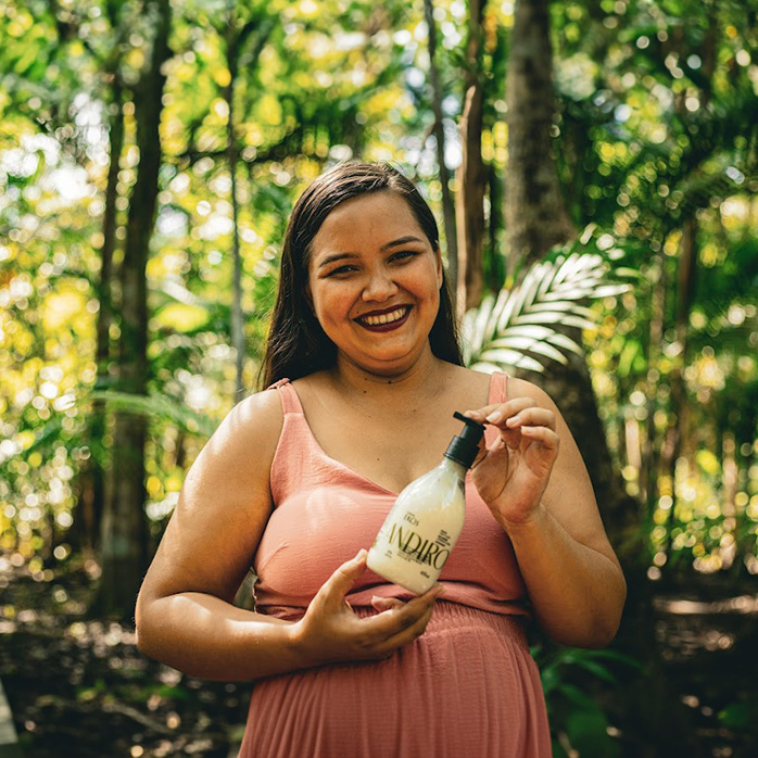 Foto de mulher, em uma floresta tropical, segurando uma Loção Corporal Natura Ekos Andiroba.