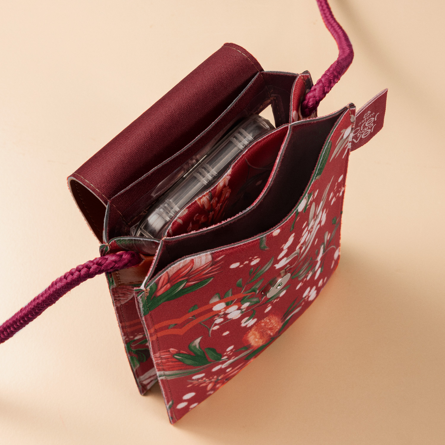 Foto com vista superior da bolsa tiracolo com porta-celular de Natura Crer para Ver mostra o produto aberto e as divisões internas. No terceiro compartimento a partir da frente está um celular.