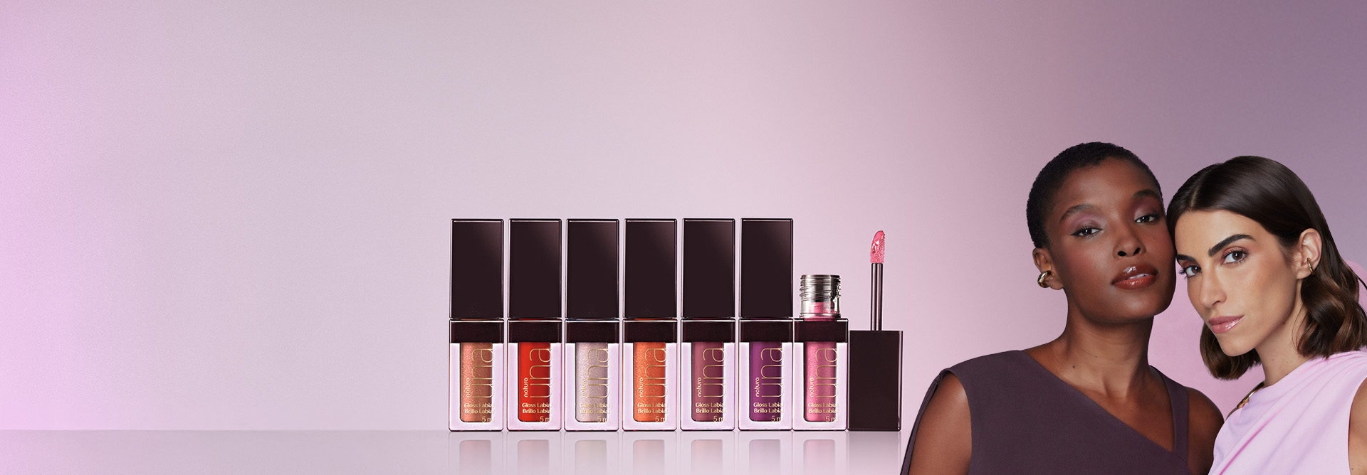 Natura Una Gloss Hidratação Ativa destaca-se no centro da tela, com as cores coral, vermelho, pérola, laranja, rosê, violeta e rosa. Á direita, modelo negra e modelo branca maquiadas com o gloss.