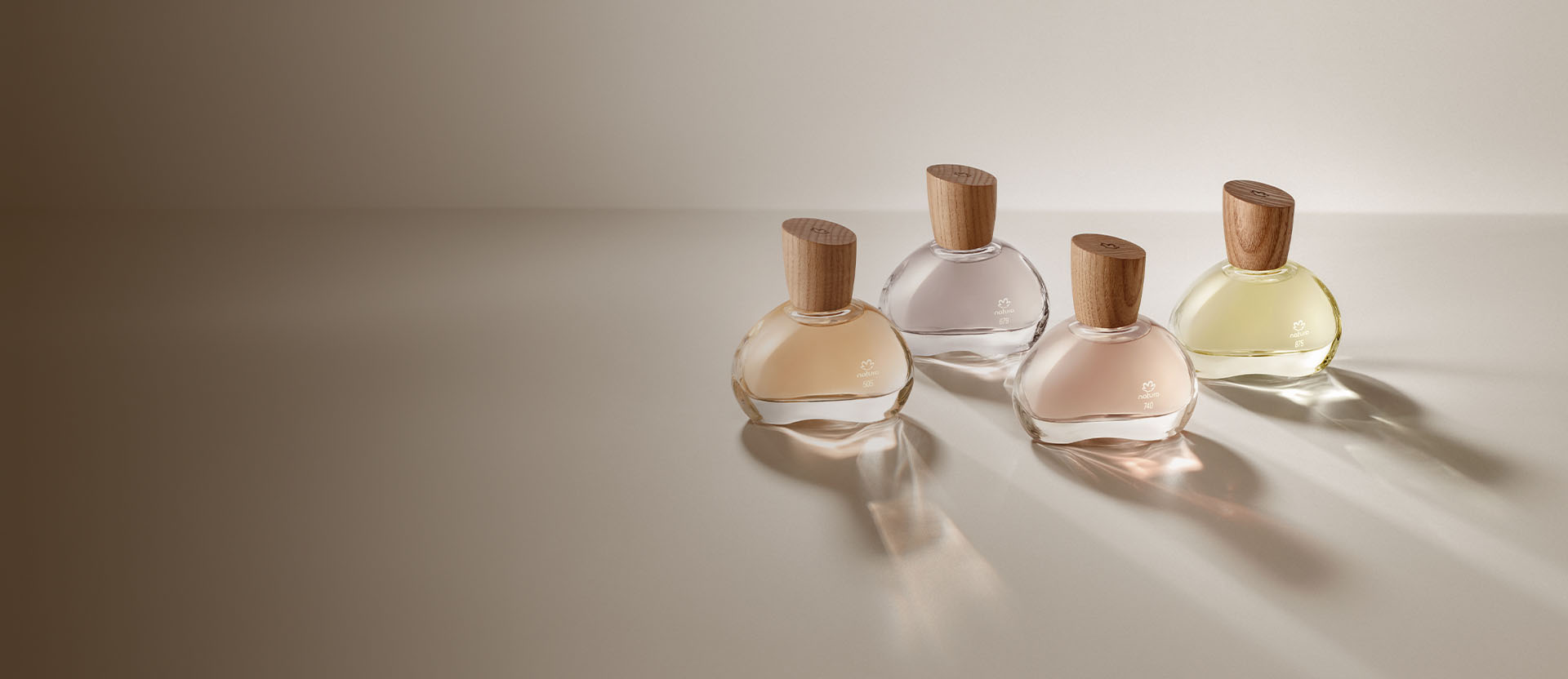 Quatro frascos de perfume com tampas de madeira, em diferentes tonalidades, dispostos em um fundo neutro.