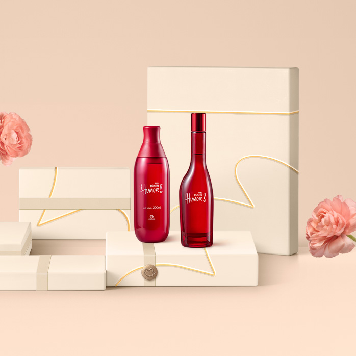 Fragrâncias Natura Meu Primeiro Humor sobre caixas presenteáveis e fundo na cor creme com flores à direita e à esquerda.