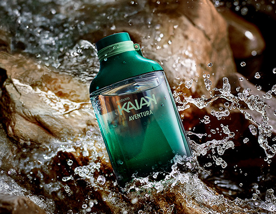 Frasco de Kaiak Aventura masculino em verde sobre pedras molhadas com água corrente e respingos.