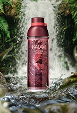Frasco de Kaiak Aventura Intensa feminino em vermelho sobre pedras na frente de uma cachoeira cercada por folhagens.