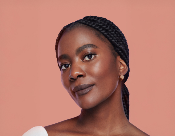 Foto de mulher negra de tranças, em fundo rosa-claro.