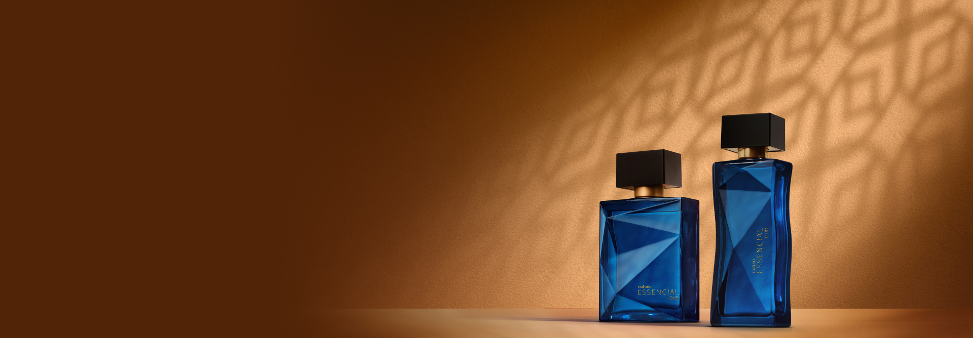 Deo Parfum Essencial Safran Masculino e Deo Parfum Essencial Safran Feminino, ambos em frascos vermelhos com tampas pretas. Estão em fundo cor areia com sombra geométrica projetada.