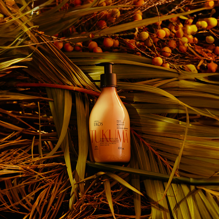 Produto Natura Ekos Tukumã sobre folhas e sementes iluminados por luz amarelada.