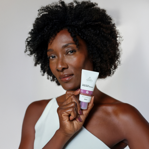 Mulher negra segura Multiprotetor FPS 70 próximo ao rosto. Ela usa blusa branca de ombro único e está em fundo branco.