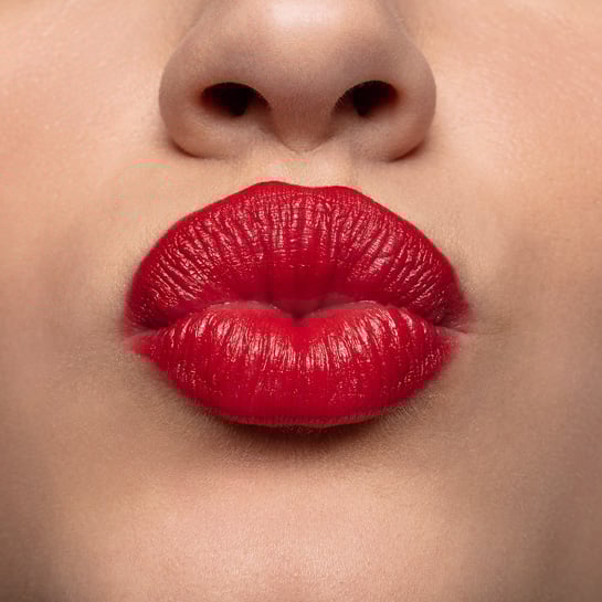 Close-up nos lábios de uma pessoa de pele branca que está fazendo gesto de beijo, com os lábios maquiados em tom vermelho vibrante.