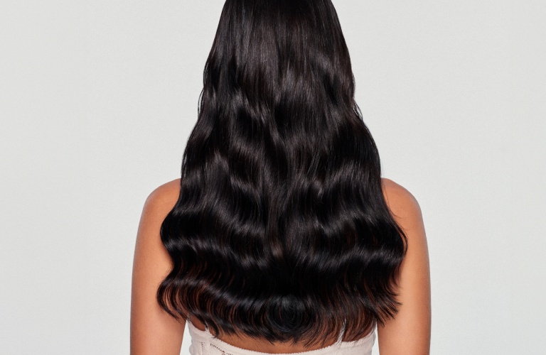 Mulher com cabelo preto ondulado longo de costas