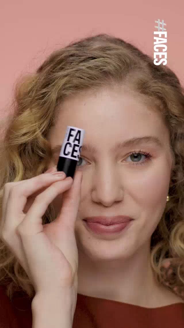 Uma mulher segura um batom multifuncional que pode ser usado também como blush. Ela passa nos lábios em frente ao rosto. O vídeo mostra outros batons em tons de rosa e vermelho com embalagens pretas e brancas e a logo "FACES" da marca.