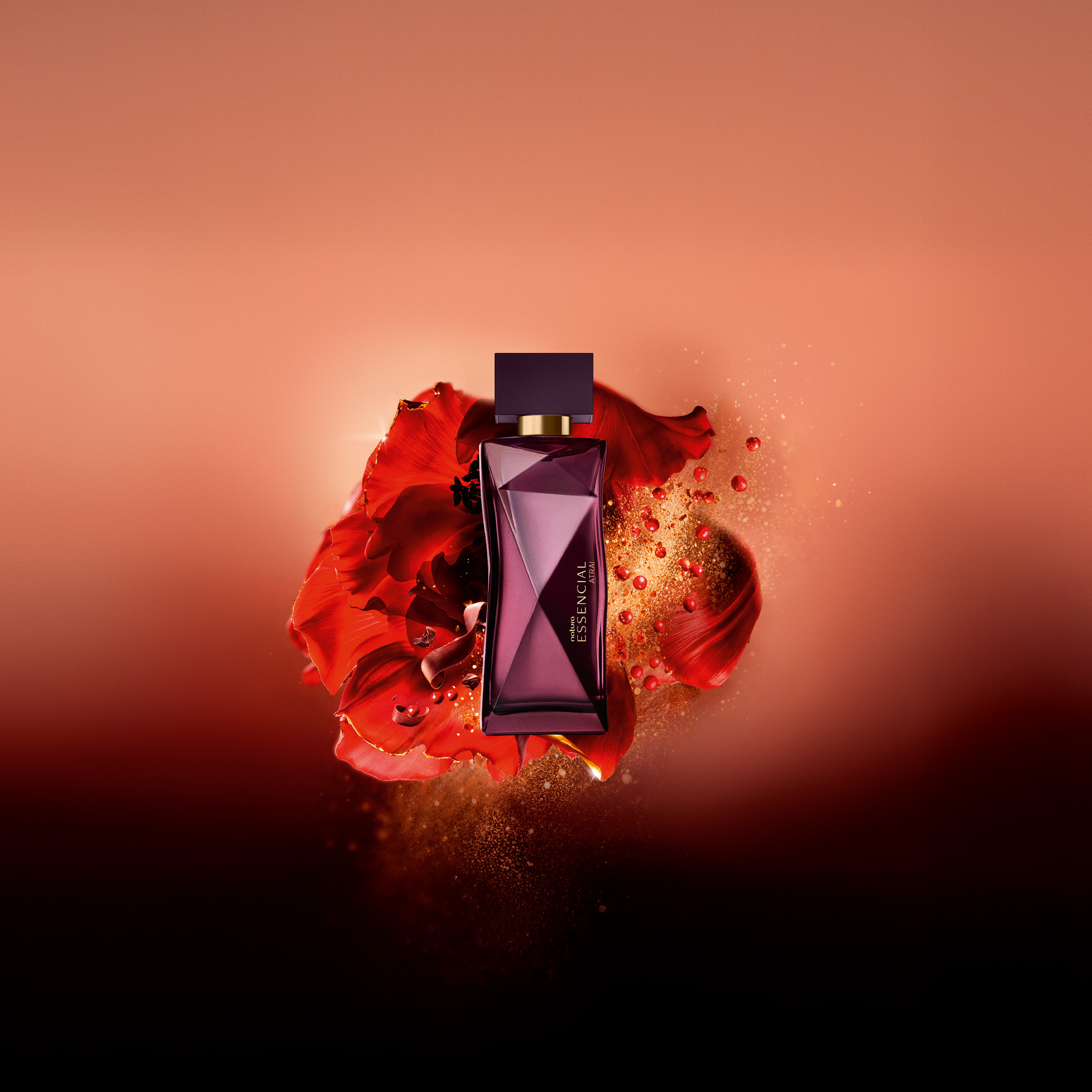 Frasco Deo Parfum Essencial Atrai Feminino em tons de vinho e dourado em destaque sobre flores vermelhas, raspas de chocolate e pimenta rosa, elementos que remetem aos ingredientes. Fundo alaranjado. 