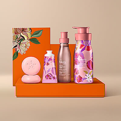 Presente Natura Tododia Flores, com Body Splash, Creme Desodorante Nutritivo para o Corpo, Creme Nutritivo para as Mãos e Sabonetes em Barra sobre caixas laranja com ilustrações florais, em fundo bege. 
