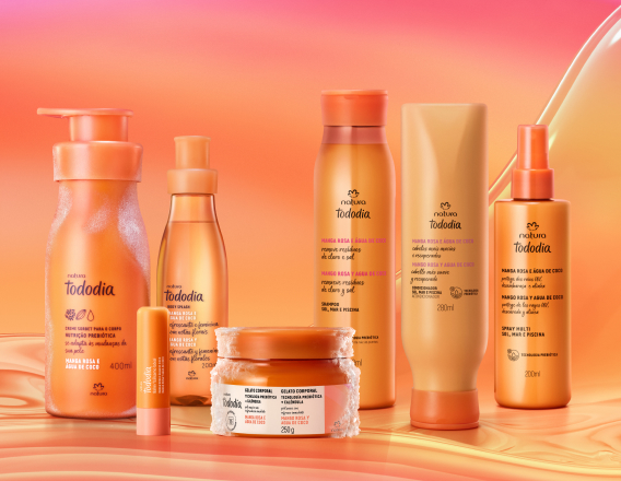 Itens Tododia Manga Rosa e Água de Coco, em laranja: frasco de Creme Sorbet, frasco de Body Splash, embalagem aberta de Balm Labial e pote de Gelato Corporal sobre grafismo e fundo em laranja.