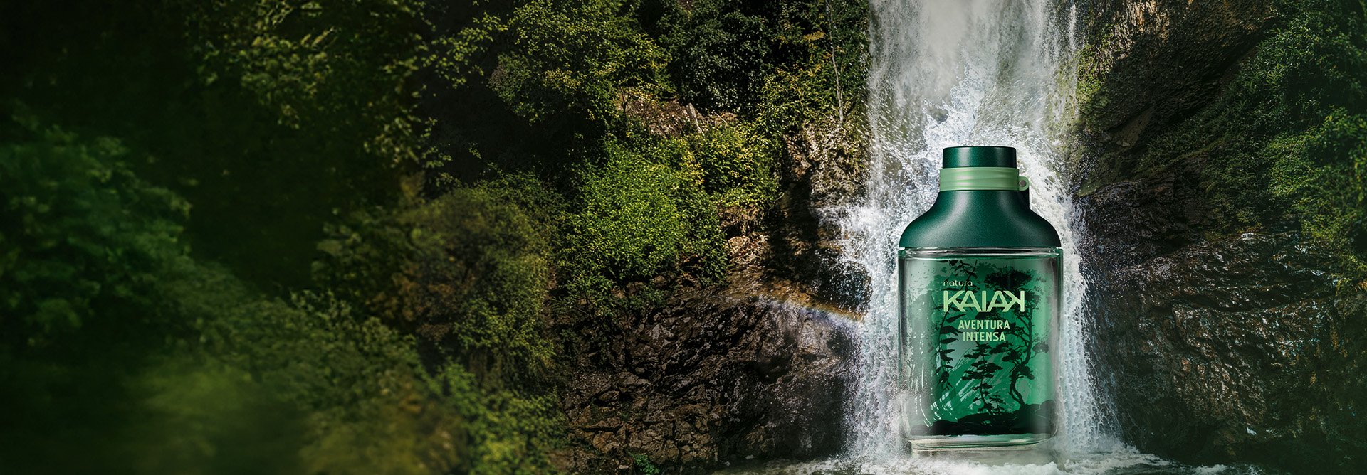 Desodorante Colônia Kaiak Aventura Intensa em frasco verde com estampa de folhagens e tampa verde-escura. O frasco está imerso na água de uma cachoeira com vegetação exuberante ao redor.