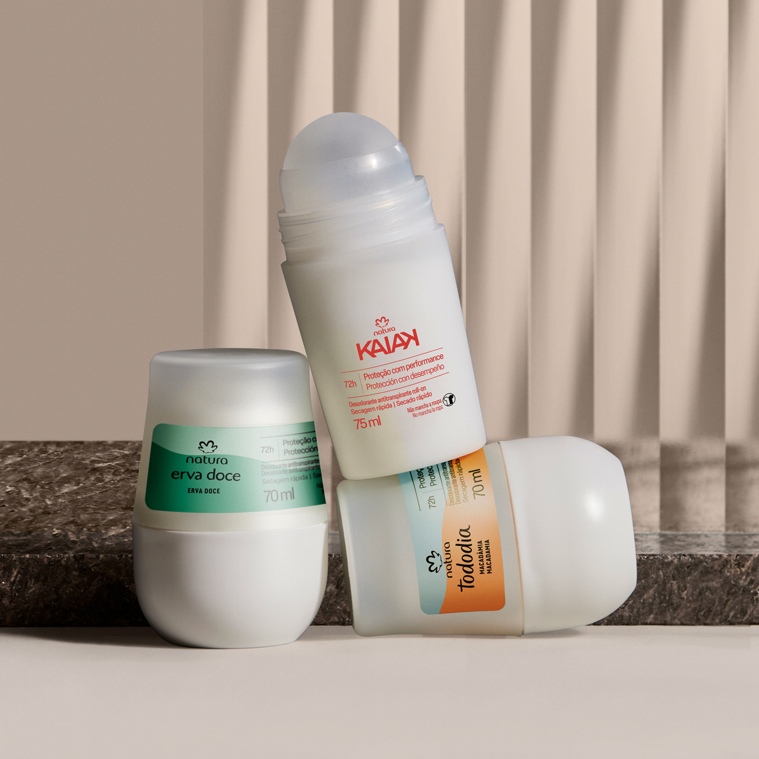 3 desodorantes roll-on da Natura, sendo 1 Erva Doce, 1 Kaiak e 1 Tododia estão empilhados diante de uma pedra de mármore cinza. Todos destacam as novas fórmulas com 72 horas de proteção. Fundo branco.
