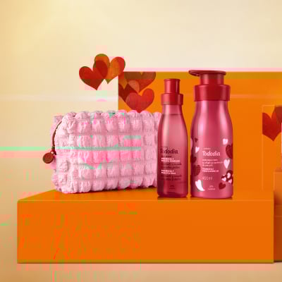 Presente Natura Tododia Framboesa e Pimenta Vermelha com Acessório: Body Splash, Creme Desodorante e Nécessaire rosa texturizado. As embalagens vermelhas estão sobre caixas de presente laranja com corações. 