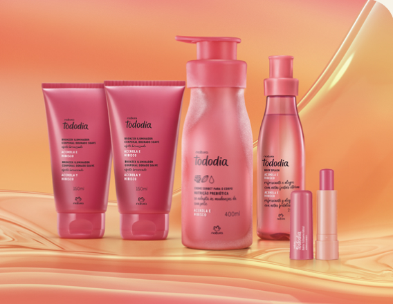 Itens Tododia Acerola e Hibisco, em rosa: bisnagas dos tons de Iluminador, frasco de Creme Sorbet, frasco de Body Splash e embalagem aberta de Balm Labial sobre grafismo e fundo em laranja.
