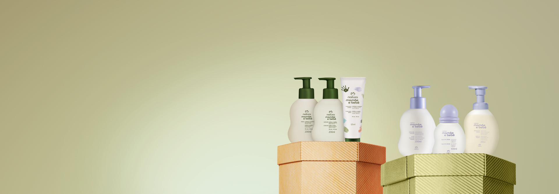 Embalagens Mamãe e Bebê sobre caixas brilhantes laranja e verde, em fundo verde: shampoo, condicionador e creme para pentear cachos e crespinhos, e sabonete líquido, colônia e sabonete líquido relaxante.