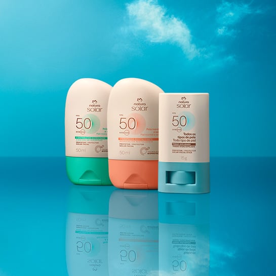 Embalagens Natura Solar Faciais FPS 50 lado a lado: creme com verde para pele mista, creme com laranja para pele normal e stick creme com azul para todos os tipos de pele, sobre fundo de céu azul.