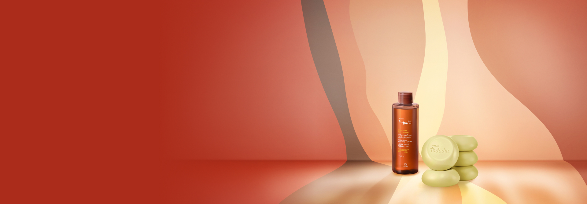 Frasco marrom do Óleo Bifásico Tododia Jambo Rosa e Flor de Caju e 5 Sabonetes em Barra Tododia. Fundo e superfície com ondas em tons de laranja, pêssego e amarelo.