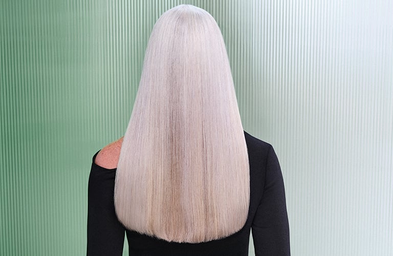 Foto de mulher de costas com cabelo platinado liso e roupa preta, em fundo verde e branco com textura vertical.