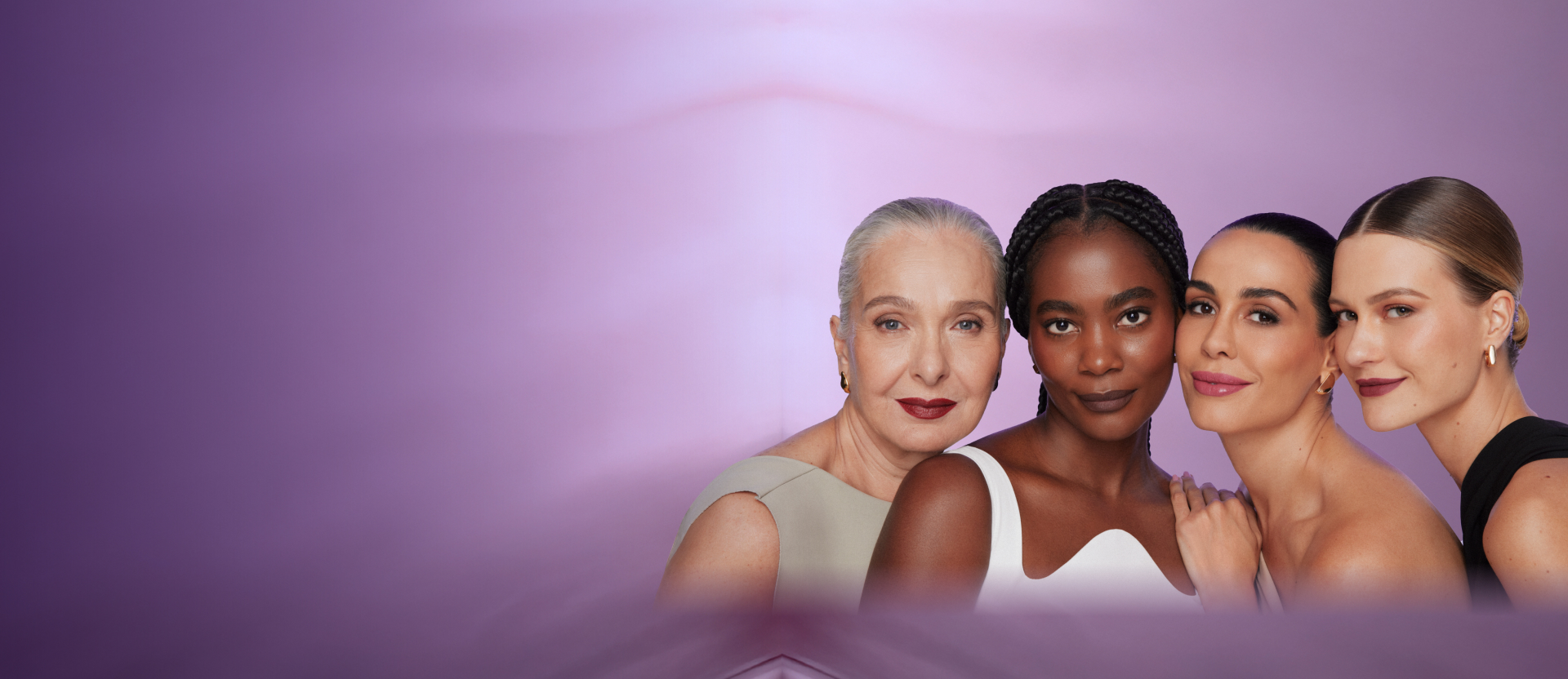 Foto de 4 modelos de diferentes idades. Todas elas estão com cabelo preso, leve sorriso no rosto, usando sombra, blush nas bochechas e batom. Fundo da imagem em degradê lilás.
