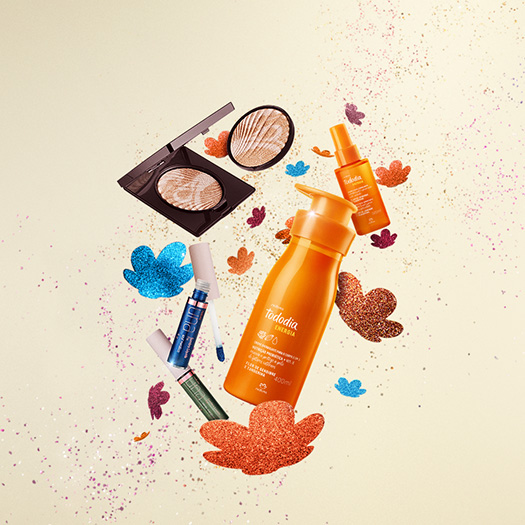 5 produtos Natura, sendo 1 Creme Nutritivo para o Corpo Tododia Energia, 1 Bruma Facial Tododia Energia, 1 Iluminador Una e 2 Sombras Líquidas Una. Fundo bege com a flor símbolo da Natura em glitter.