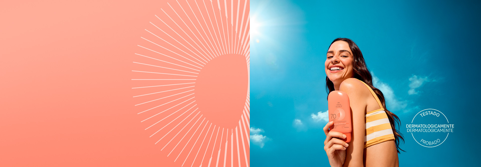 Mulher de cabelos castanhos segura próximo ao corpo embalagem laranja de Natura Solar Corporal FPS 70. Fundo de céu azul com selo branco circular “Testado Dermatologicamente” e grafismo branco. Base da imagem com faixa laranja.
