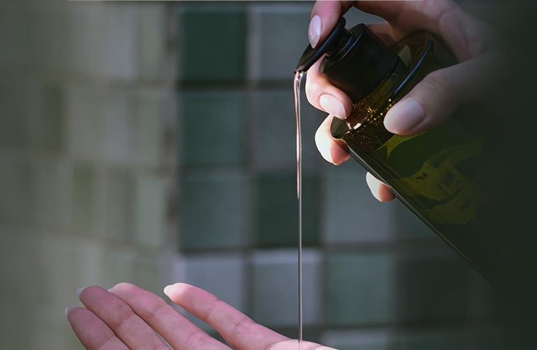 Uma mão apertando o pump de um sabonete líquido, que cai no ar em direção a outra mão