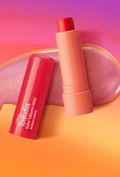 Embalagem rosada aberta de Balm Labial Tododia Acerola e Hibisco sobre textura rosada cremosa, em fundo em tons de laranja e rosa.