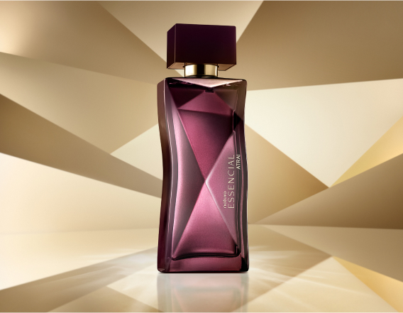 Frasco de Essencial Atrai Feminino, em tons de roxo, aparece em destaque no centro da tela sobre fundo multifacetado dourado, fazendo alusão ao design do frasco de Essencial.
