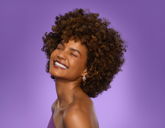 Foto de mulher de cabelos curtos e cacheados sorrindo, em fundo roxo.