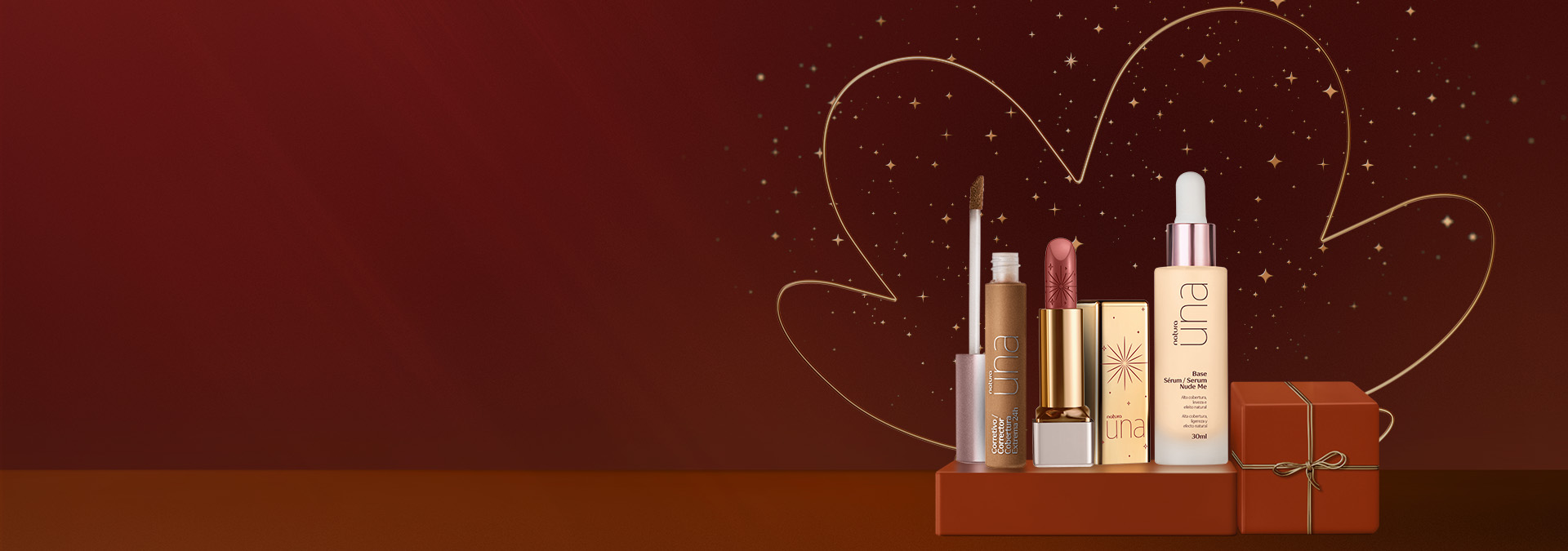 Maquiagens Natura Una: Corretivo aberto, Batom com tampa aberta dourada e Base Sérum, sobre caixas de presente marrom com fita dourada. Fundo vinho com flor símbolo da Natura e pontos de luz dourados.