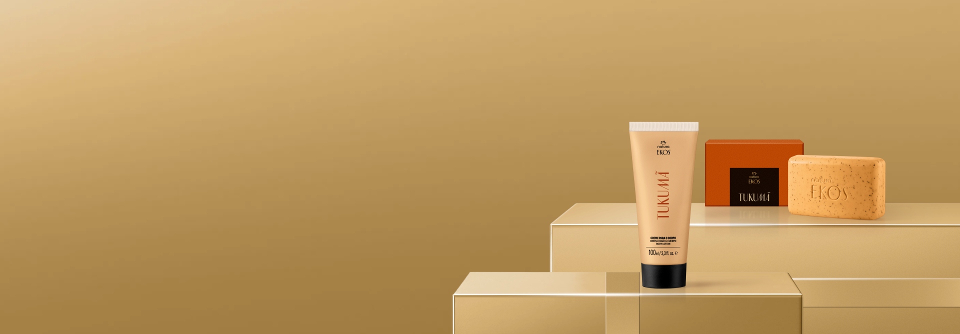 Creme para o Corpo e Caixa de Sabonete em Barra da linha Ekos Tukumã. Os produtos estão sobre caixas douradas com laços da mesma cor em um fundo bege. 