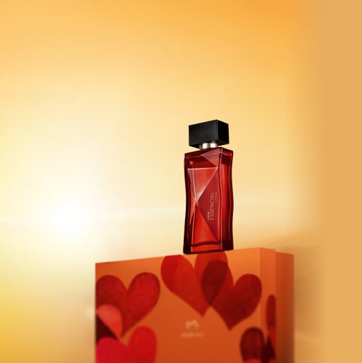 Frasco de vidro vermelho com tampa preta do Deo Parfum Essencial Safran Feminino em destaque sobre caixa de presente laranja com corações vermelhos, em fundo degradê amarelo.