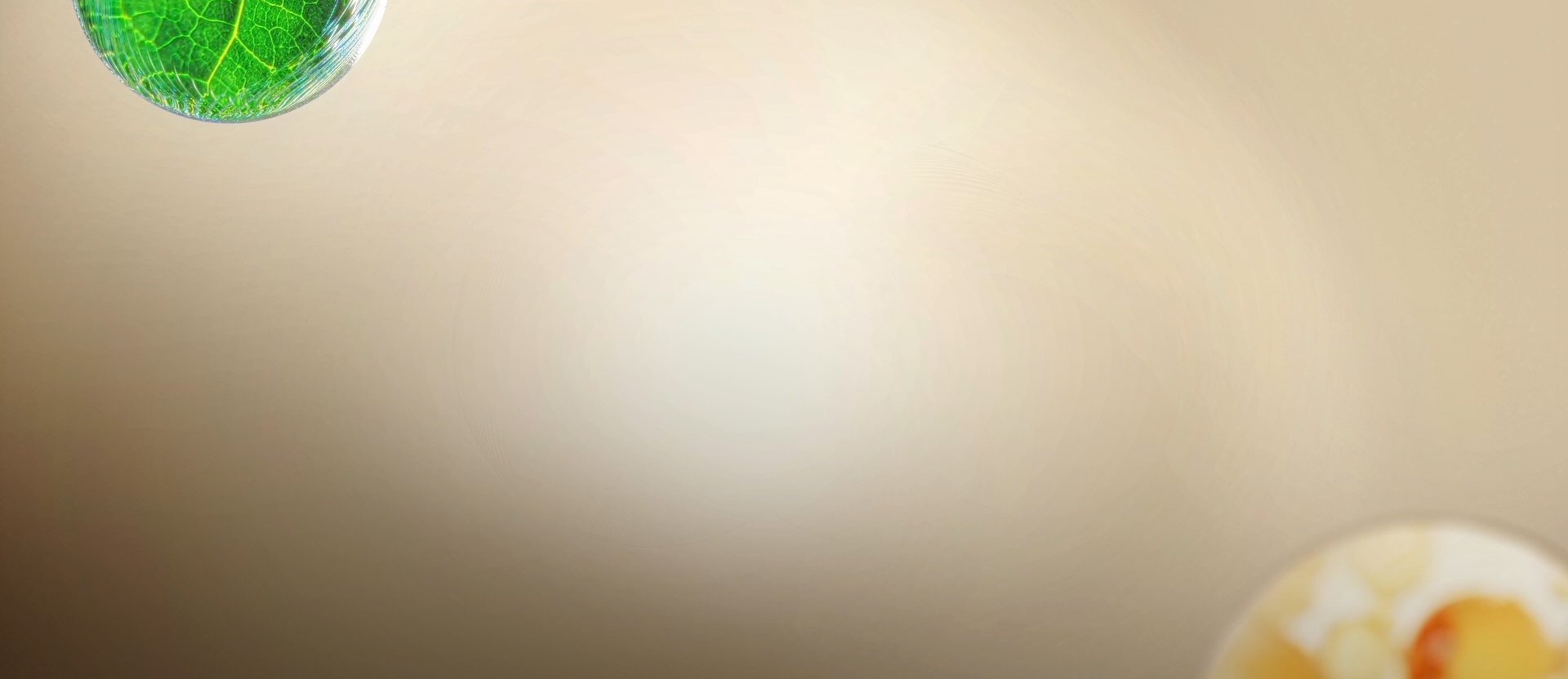 Vídeo mostrando duas esferas translúcidas se aproximando. A verde, com textura de folhas, e a dourada, com pequenas cápsulas dentro, se encontram, simbolizando a fusão de ingredientes.