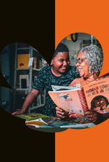 Imagem de uma senhora sorridente de cabelos grisalhos e óculos, lendo um livro com o título "Menina Bonita do Laço de Fita" em voz alta para um jovem com um sorriso, que a abraça gentilmente por trás. Ambos estão em uma biblioteca, com estantes de livros ao fundo, e a cena é emoldurada por um fundo em preto e laranja.