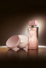 Na cena, Desodorante Hidratante Corporal Perfumado Essencial Feminino e Deo Parfum Essencial Feminino aparecem iluminados sobre superfície marrom em fundo escuro.